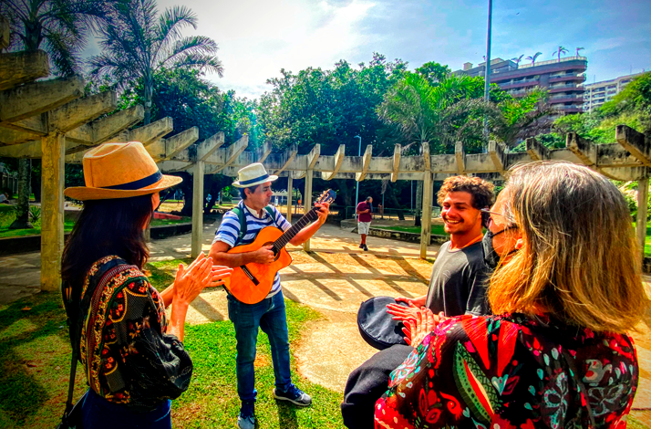 A musician performing with a guitar during an outdoor gathering in Rio de Janeiro, surrounded by tour participants in a landscaped urban park setting.