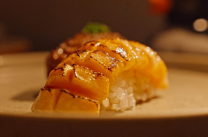 This close-up captures a piece of beautifully seared, diamond-cut nigiri sushi from the menu at Kokoro Hand Roll Bar in Dubai.