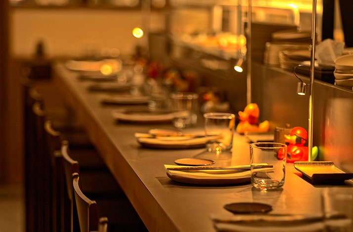 Sushi counter setup with plates, water glasses, and bright orange rubber ducks at Kokoro Hand Roll Bar, Dubai.