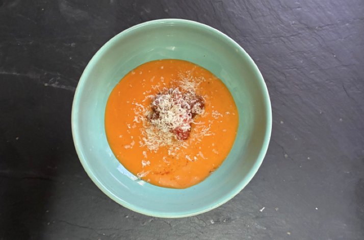 Creamy orange soup topped with grated cheese and meat garnish served in a mint-green bowl at O Balado.