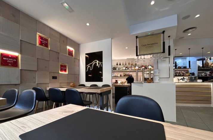 Interior of Casa Barqueiro showing Michelin 2024 awards on the wall, navy seating, a bar with glassware, and restaurant logo signage.