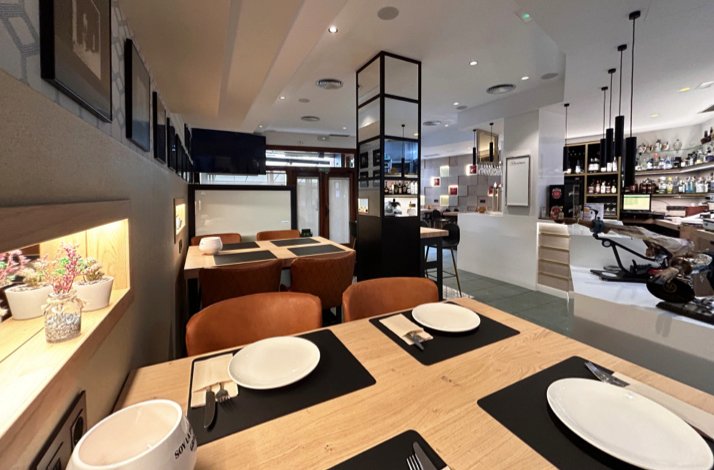 Casa Barqueiro restaurant interior showing wooden tables with black placemats, tan leather chairs, and a well-stocked bar area.
