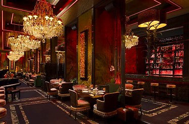 Dimly lit dining room at Sass' Restaurant & Lounge featuring ornate chandeliers, glowing bar shelves, and velvet seating.