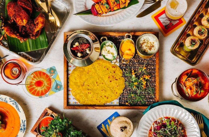 Vibrant Indian spread displayed from above, showcasing flatbread, shrimp curry, grilled paneer, chutneys, and drinks.