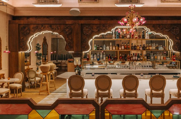 Backlit bar shelving stocked with spirits beneath carved wooden arches.