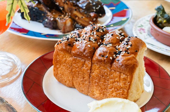 Close-up of a glossy sesame-topped pull-apart bread loaf on a plate, with butter alongside, served at Prubechu.