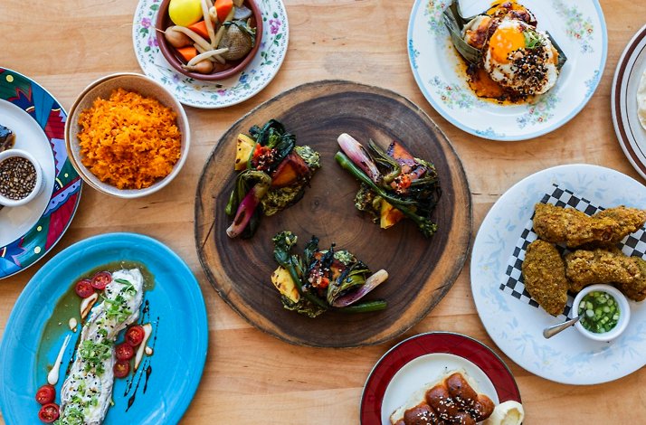 Overhead spread of plated dishes including orange rice, fried chicken, greens, and sauced entrées served at Prubechu.
