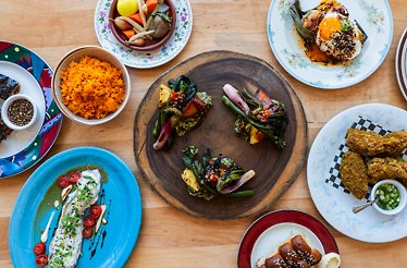 Overhead spread of plated dishes including orange rice, fried chicken, greens, and sauced entrées served at Prubechu.
