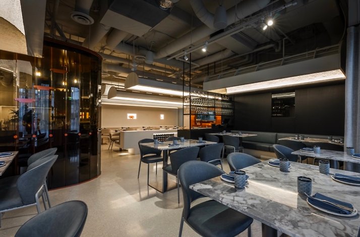 ELEM restaurant's casual dining area featuring oak tables, grey banquette seating, wishbone chairs, and floor-to-ceiling windows.