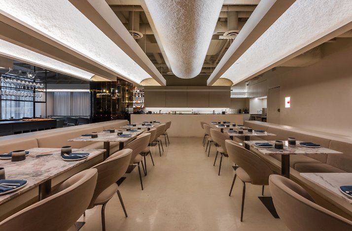 ELEM restaurant's warmly lit dining room featuring marble-topped tables, taupe chairs, and a glowing copper-accented open kitchen.