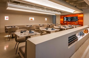 ELEM restaurant's moody cocktail bar area with slate-blue chairs, marble tables, a curved mirrored column, and suspended glassware.