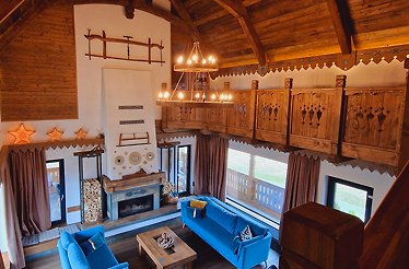 Traditional Transylvanian interior at Plai din Bran with blue velvet sofas, lit chandelier, and ornate carved wood balcony.