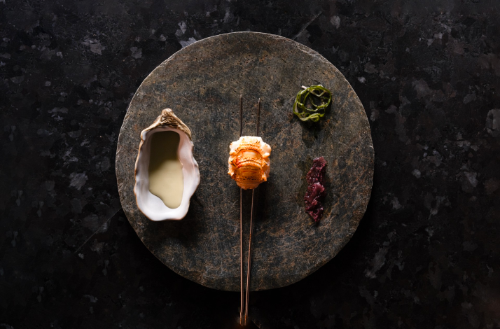 Exquisite seafood course served on a dark stone plate with oyster shell sauce.