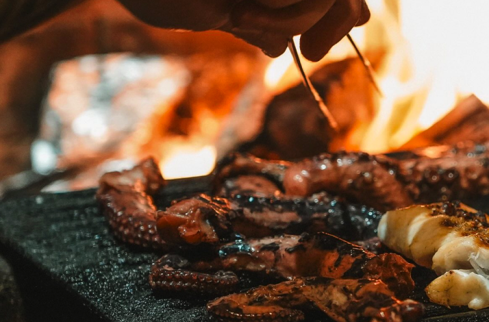 Fresh octopus tentacles sizzling and being grilled over open flames.