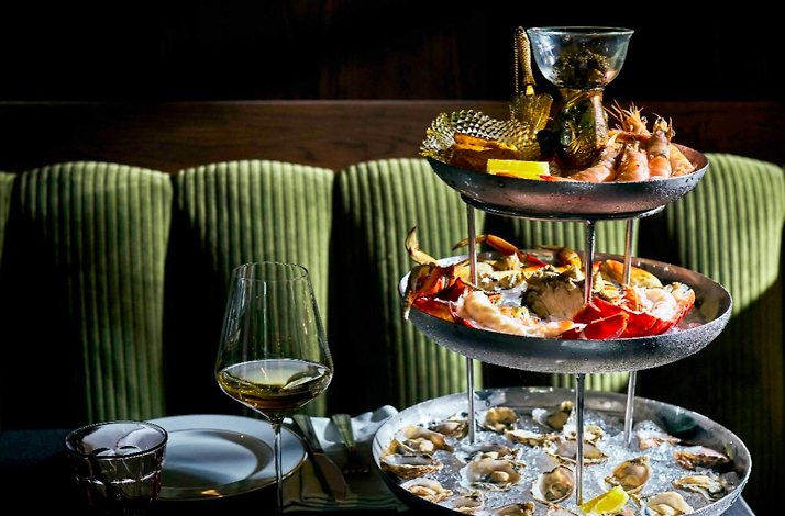 JouJou's seafood tower featuring fresh oysters, whole crab, prawns, and caviar vessel across three tiers, paired with chilled white wine.