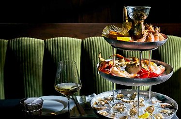 JouJou's seafood tower featuring fresh oysters, whole crab, prawns, and caviar vessel across three tiers, paired with chilled white wine.