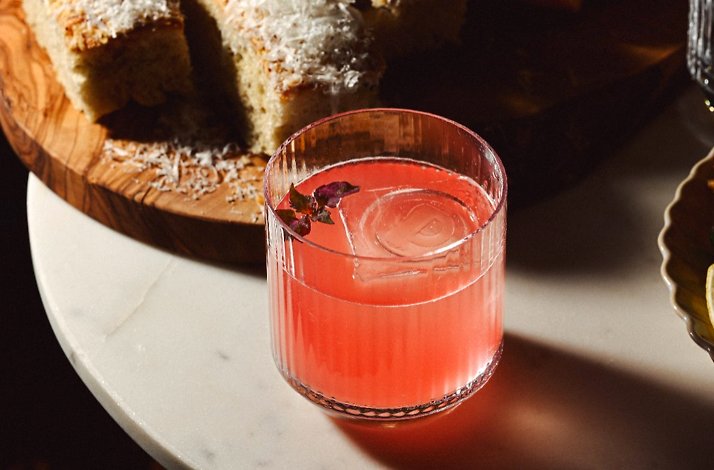 Pink cocktail garnished with dried rose petals, served alongside focaccia on a marble surface at La Padrona Boston.