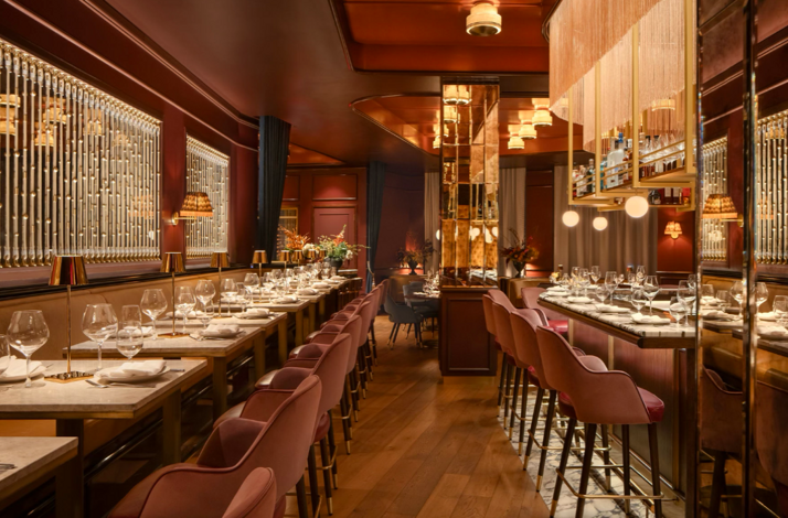  La Padrona Boston dining room featuring rose-pink bar stools, gold-toned mirrors, and crystal wall accents under warm lighting.