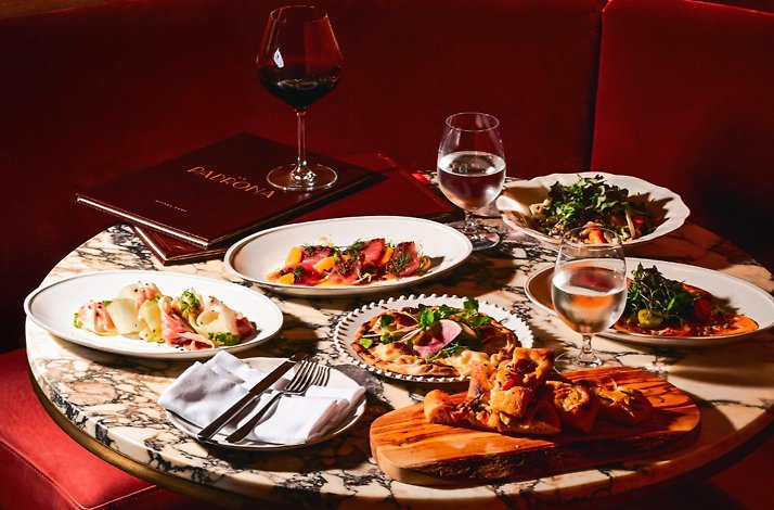 La Padrona Boston marble table set in a red velvet booth, displaying Italian antipasti, flatbreads, salads, and wine.