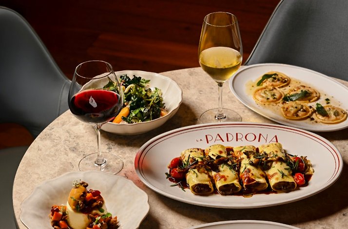 La Padrona Boston table set with cannelloni on a branded platter, ravioli, greens, and red and white wines.