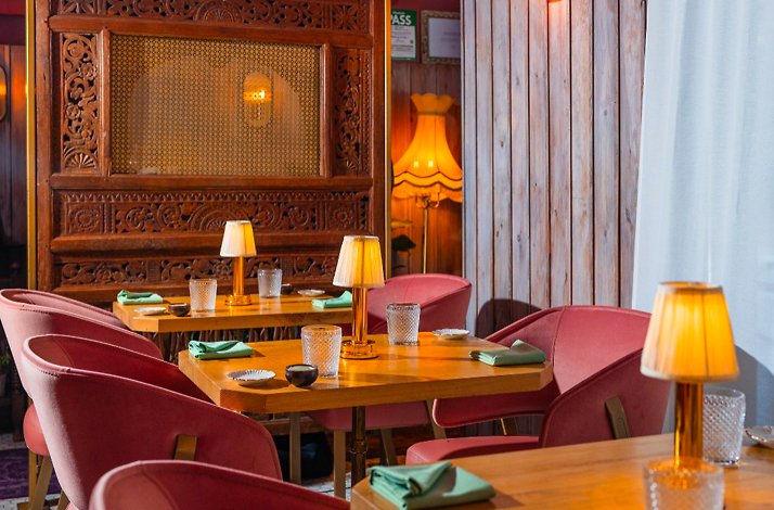 Intimate Kiin dining room featuring pink velvet chairs, wooden tables with table lamps, and carved Thai wooden panels.
