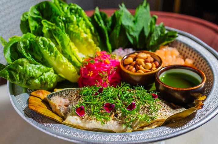 Thai-style whole fish platter arranged with greens, edible flowers, roasted peanuts, and green herb sauce.