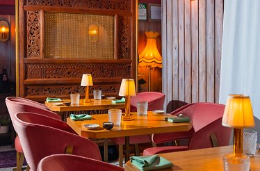 Intimate Kiin dining room featuring pink velvet chairs, wooden tables with table lamps, and carved Thai wooden panels.