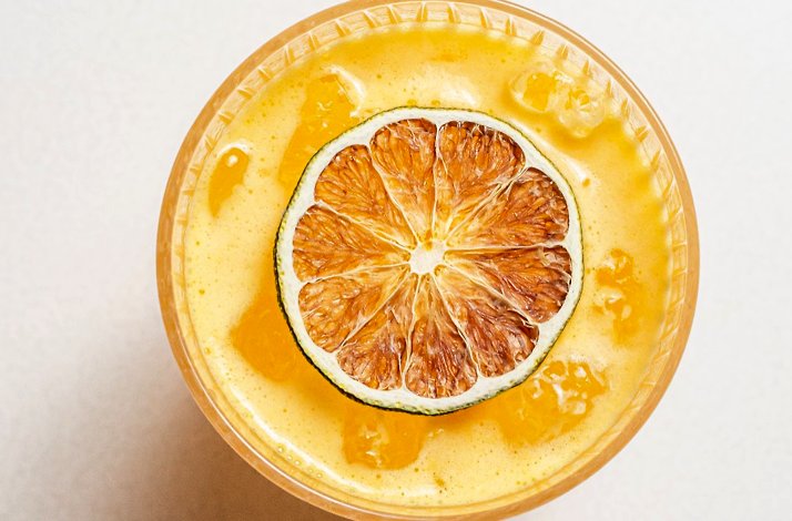 Overhead view of a golden frothy cocktail in a coupe glass garnished with a charred lime half at Le Jardinier.