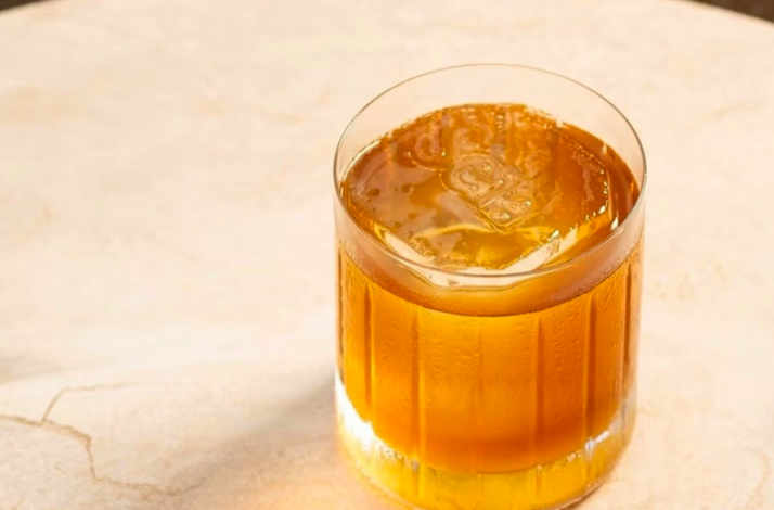 An Old Fashioned cocktail served in a paneled rocks glass with a large clear ice cube.