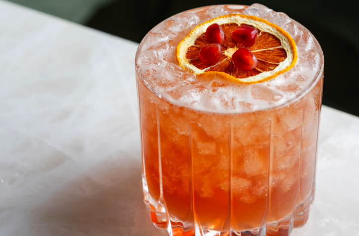 Iced citrus cocktail with a dried orange wheel and pomegranate arils at Le Jardinier Houston.