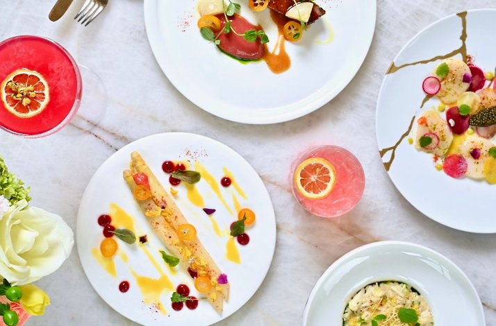 Overhead view of elegant plated dishes and pink cocktails on a marble table at Le Jardinier Houston.