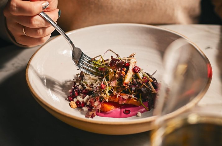 A plated salad with roasted vegetables, microgreens, and a vibrant pink puree, served in a wide ceramic bowl.