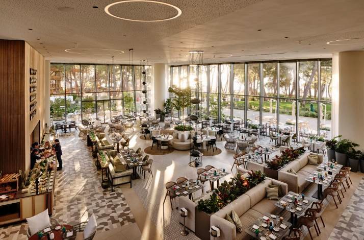 Bright restaurant with floor-to-ceiling windows, buffet station, and neatly set tables in a spacious, modern dining room.