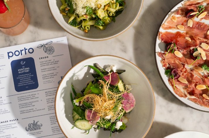 Porto Boston's Winter 2026 menu alongside shared plates including green pasta, a salad, prosciutto, and a pink cocktail.