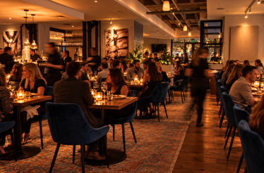 Porto Boston's candlelit dining room filled with guests at wooden tables with blue velvet chairs during a busy evening service.