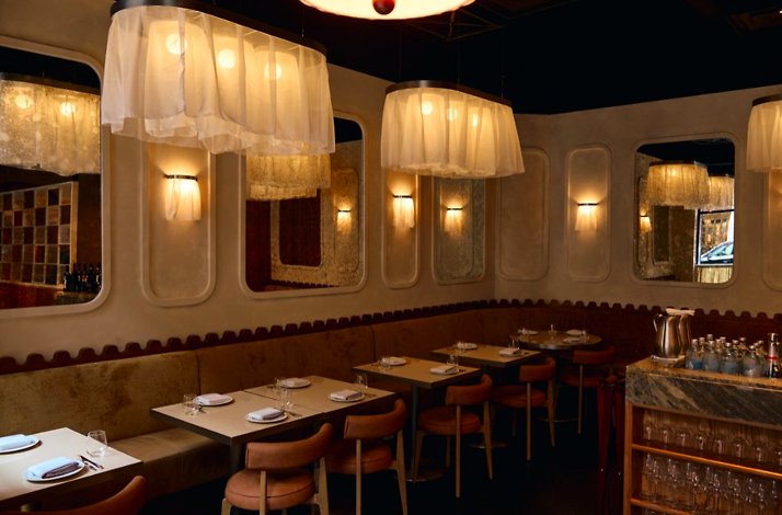 Banquette dining area with set tables, mirrored walls, and soft pendant lamps at Eloise.