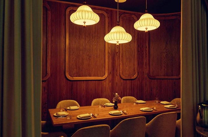 Private dining room with a long set table, wood-paneled walls, and three pendant lights at Eloise.