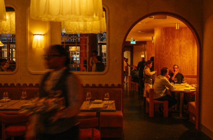 Warm dining room view through an arched doorway with diners and candlelit tables at Eloise.