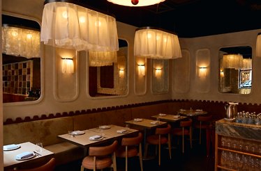 Banquette dining area with set tables, mirrored walls, and soft pendant lamps at Eloise.