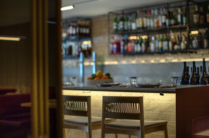 Intimate bar seating at Giuletta with woven-back stools and softly backlit liquor shelves.