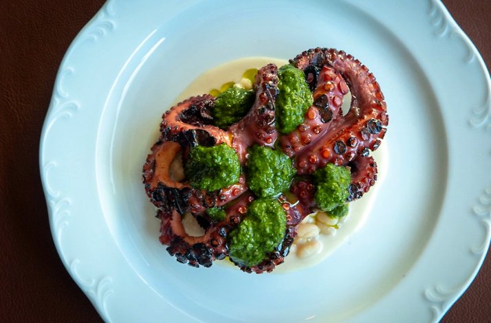 Grilled octopus at Giuletta topped with bright green herb sauce on a white plate.