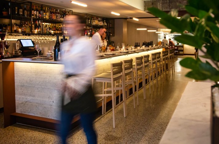 Giuletta’s long, warmly lit bar with bottles on open shelving and a server passing by.