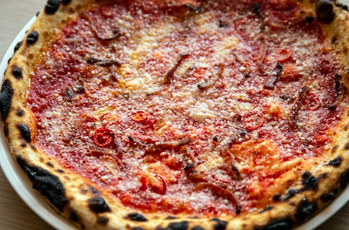 Thin-crust pizza at Giuletta with tomato sauce, grated cheese, chili slices, and charred edges.