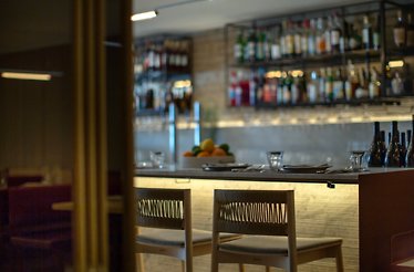 Intimate bar seating at Giuletta with woven-back stools and softly backlit liquor shelves.