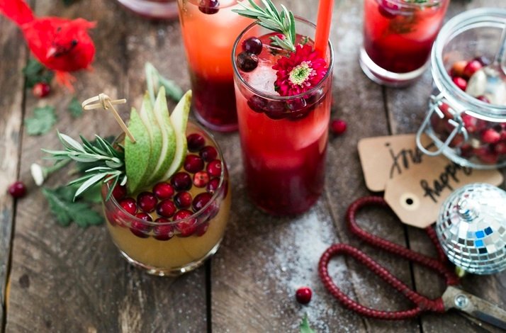 Festive holiday drinks garnished with cranberries, rosemary, pear slices, and a flower on a rustic wooden table.