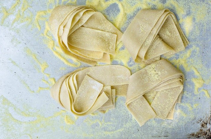 Four fresh pappardelle pasta nests dusted with semolina flour at a Dublin Cookery School culinary workshop.