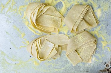 Four fresh pappardelle pasta nests dusted with semolina flour at a Dublin Cookery School culinary workshop.