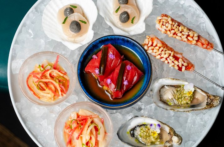 Takja's chilled seafood platter with oysters, scallops, prawn skewers, tuna, and Korean banchan arranged on crushed ice.