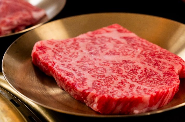 Close-up of a thick, finely marbled dry-aged beef slice displayed on a polished brass plate.