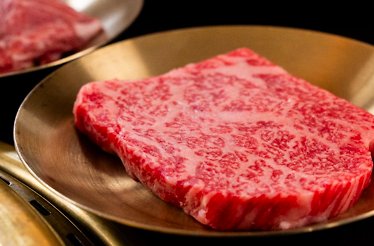 Close-up of a thick, finely marbled dry-aged beef slice displayed on a polished brass plate.